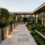 Aménagement extérieur : 8 éléments à harmoniser pour un projet réussi Terrasse et jardin contemporains haut de gamme avec allée élégante, végétation structurée et lumière douce en fin de journée, ambiance extérieure harmonieuse.
