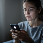 Quel service gratuit est le plus fiable pour identifier un appelant ? Femme consultant un smartphone après avoir remarqué un appel manqué, dans une ambiance intérieure réaliste et sobre.